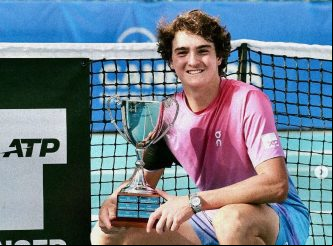 Jovem tenista com troféu ATP ao lado da rede